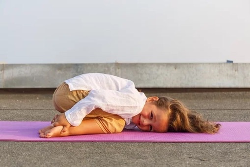 Child resting in a gentle yoga pose on a mat outdoors
